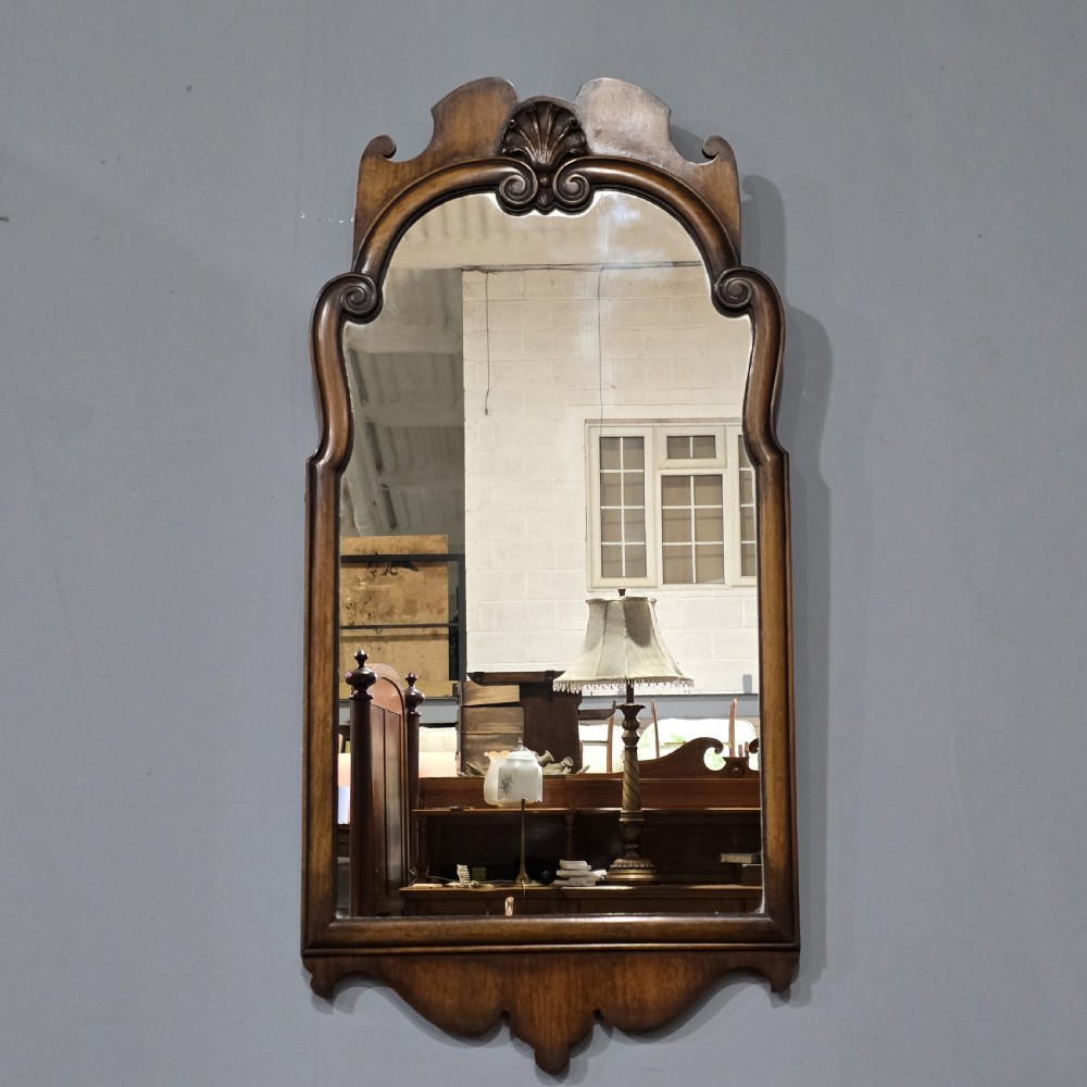 A portrait wall mirror in a dark walnut timber frame featuring an arched top and a carved scallop shell cresting.