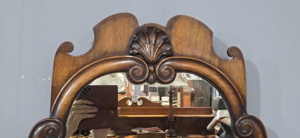 A portrait wall mirror in a dark walnut timber frame featuring an arched top and a carved scallop shell cresting. View V