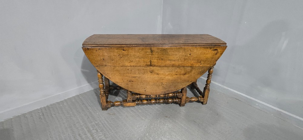 An 18th-century oak drop-leaf dining table featuring turned legs, lower stretchers, and a carved end frieze. View II