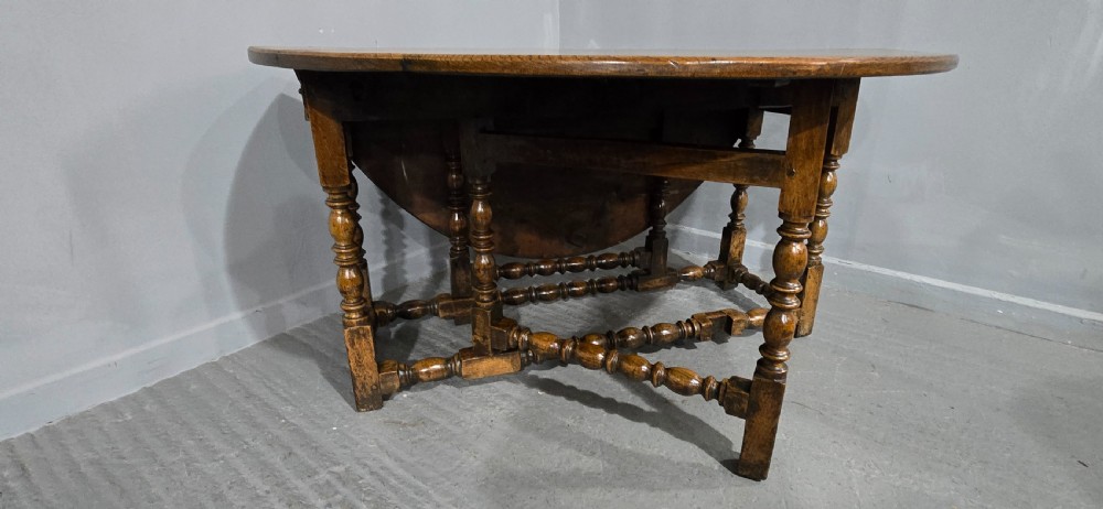 An 18th-century oak drop-leaf dining table featuring turned legs, lower stretchers, and a carved end frieze. View III