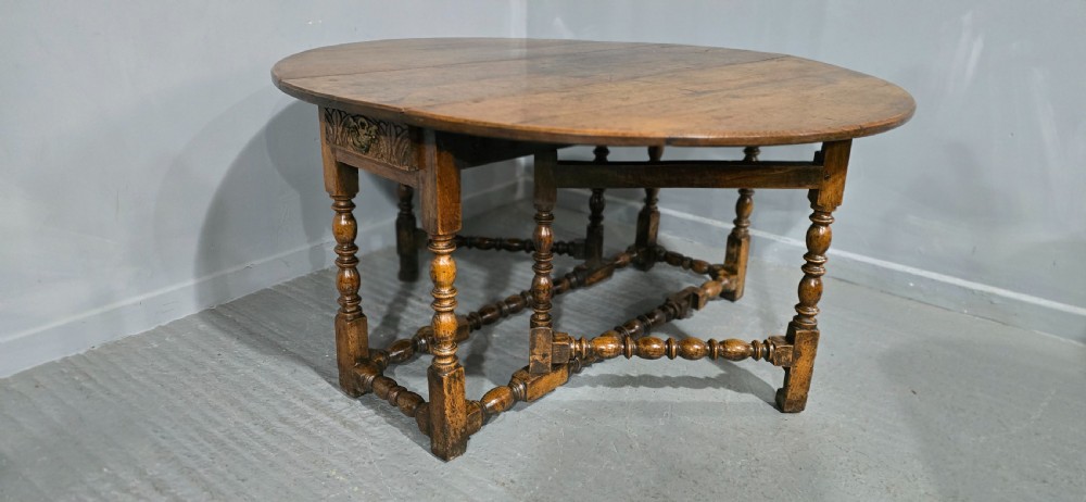 An 18th-century oak drop-leaf dining table featuring turned legs, lower stretchers, and a carved end frieze. View V