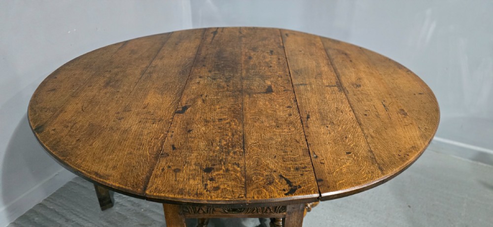 An 18th-century oak drop-leaf dining table featuring turned legs, lower stretchers, and a carved end frieze. View IX