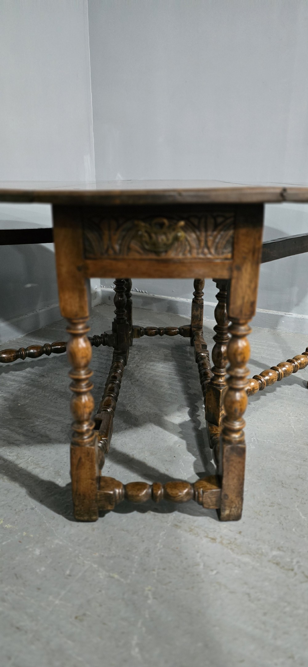 An 18th-century oak drop-leaf dining table featuring turned legs, lower stretchers, and a carved end frieze. View X