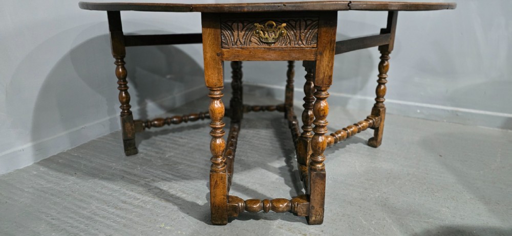 An 18th-century oak drop-leaf dining table featuring turned legs, lower stretchers, and a carved end frieze. View XII
