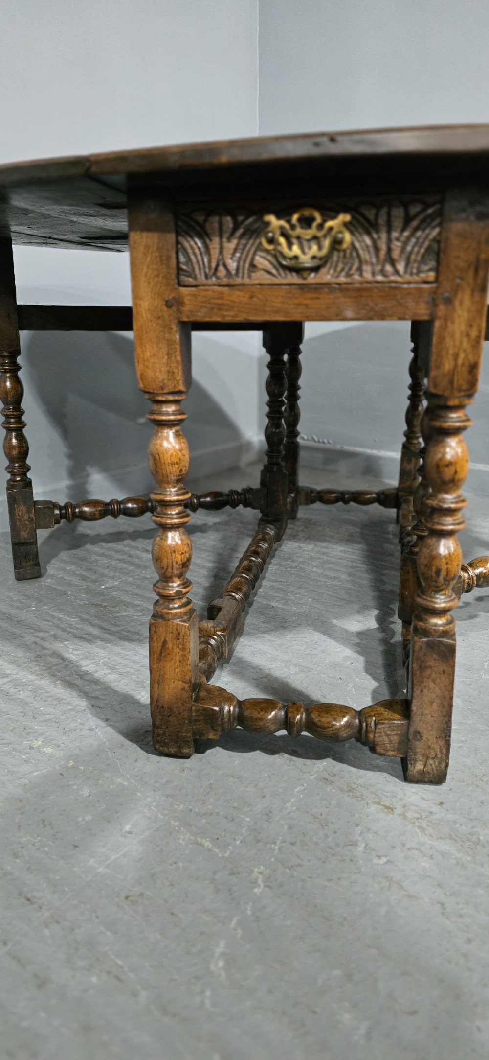An 18th-century oak drop-leaf dining table featuring turned legs, lower stretchers, and a carved end frieze. View XIII