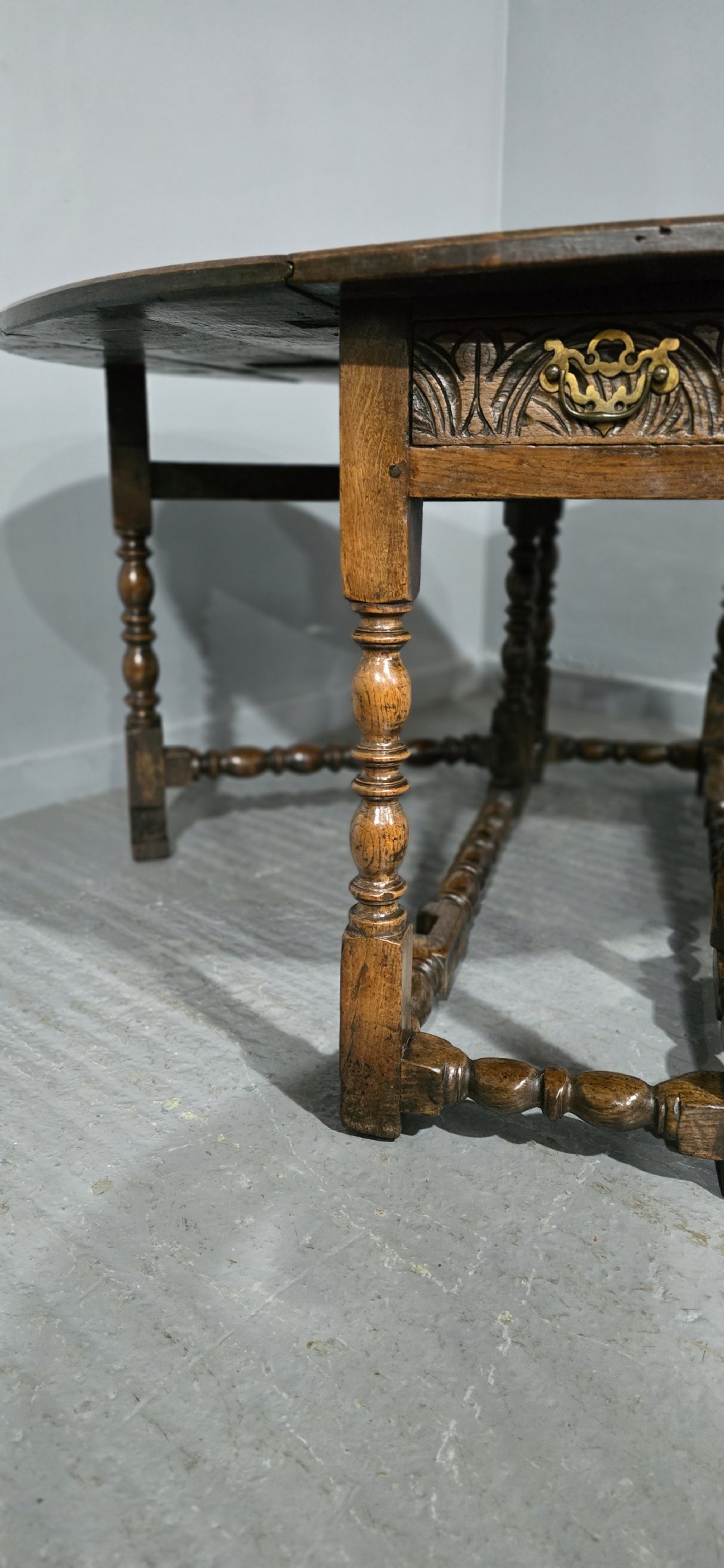 An 18th-century oak drop-leaf dining table featuring turned legs, lower stretchers, and a carved end frieze. View XIV