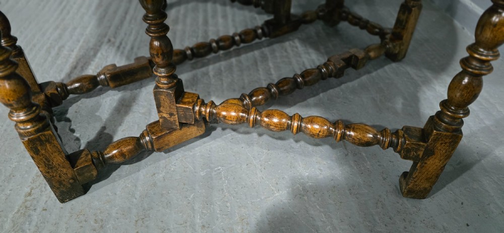 An 18th-century oak drop-leaf dining table featuring turned legs, lower stretchers, and a carved end frieze. View XV