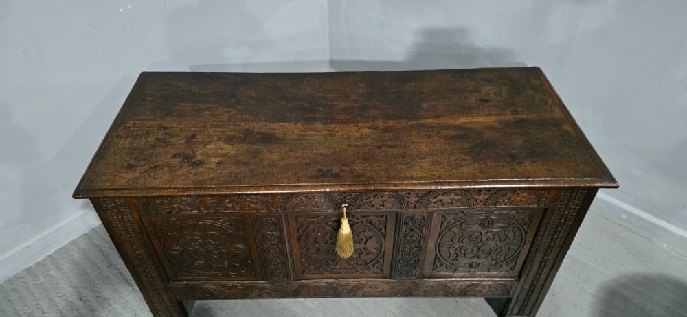 A 17th-century dark oak coffer with three hand-carved front panels and a flat rectangular hinged top. View II