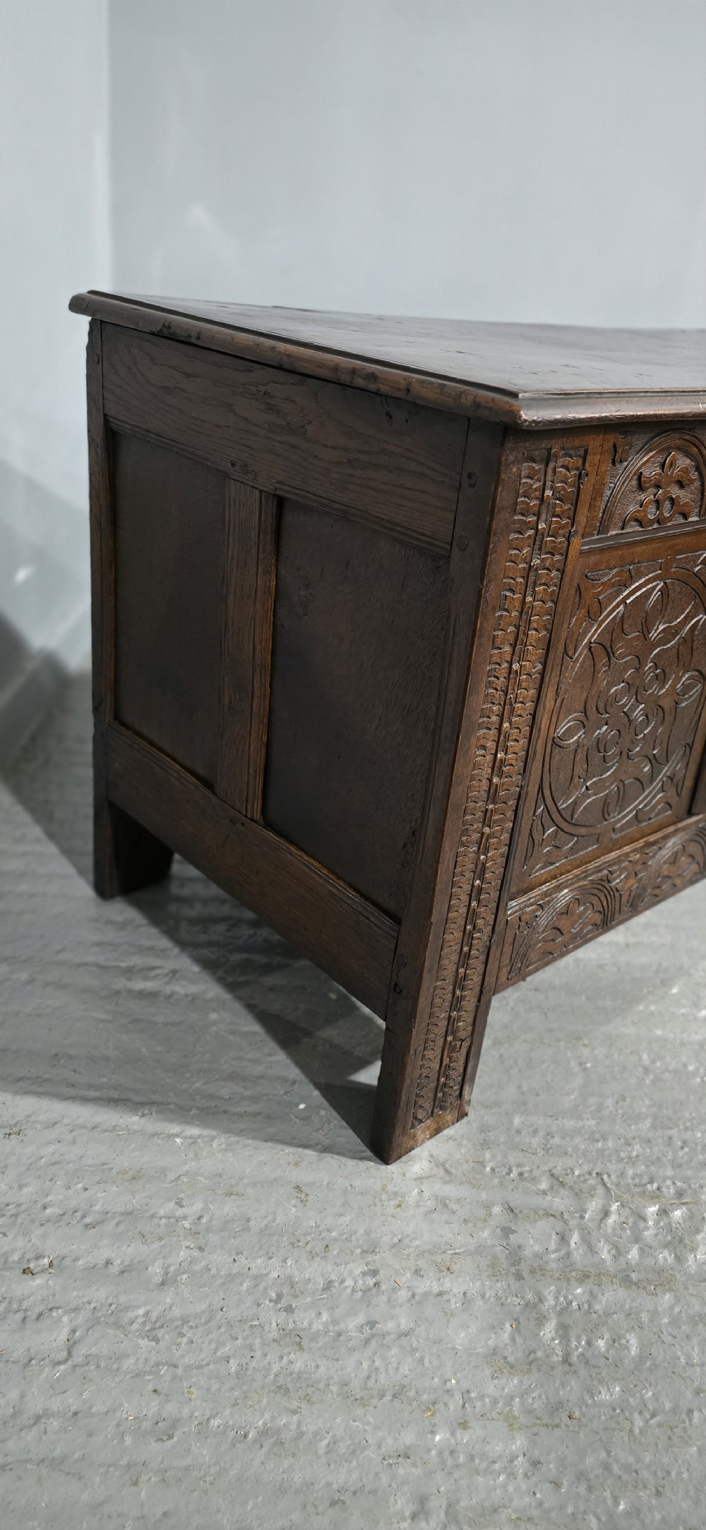 A 17th-century dark oak coffer with three hand-carved front panels and a flat rectangular hinged top. View V