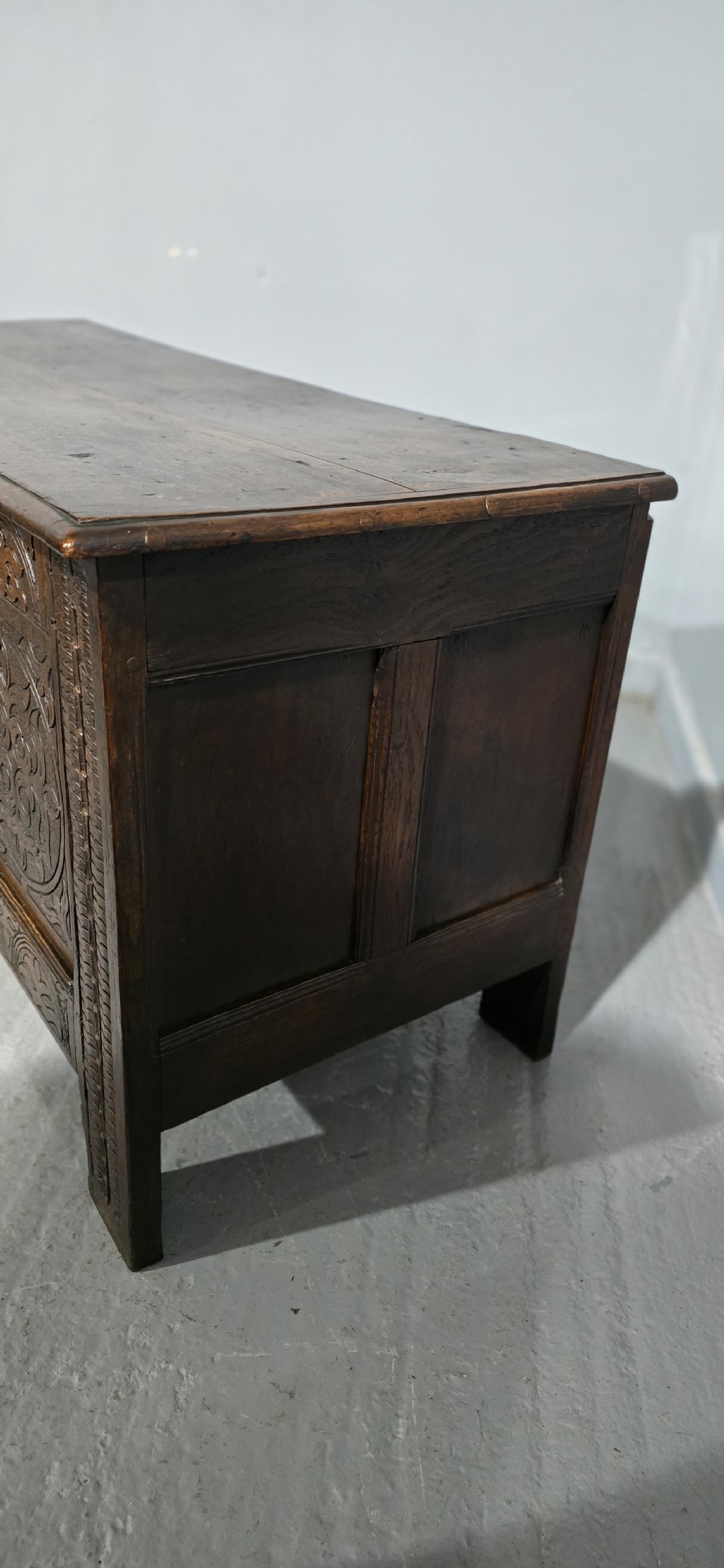 A 17th-century dark oak coffer with three hand-carved front panels and a flat rectangular hinged top. View VI