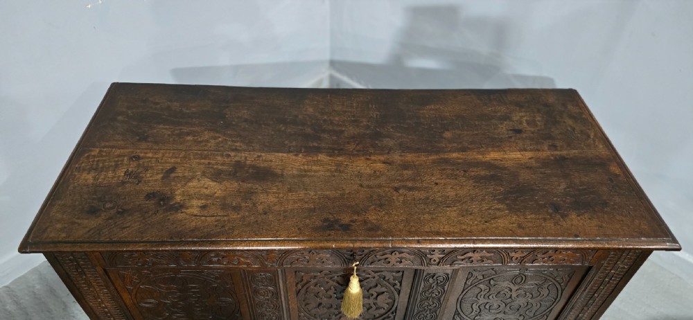 A 17th-century dark oak coffer with three hand-carved front panels and a flat rectangular hinged top. View IX