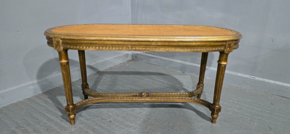 An oval French Louis XVI style duet stool featuring a carved giltwood frame with fluted legs and a gold silk satin upholstered cushion. View III