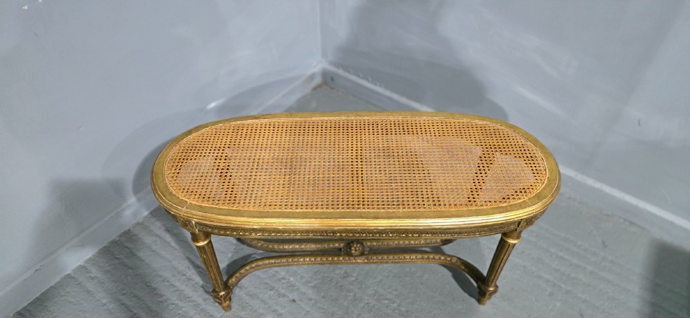 An oval French Louis XVI style duet stool featuring a carved giltwood frame with fluted legs and a gold silk satin upholstered cushion. View V