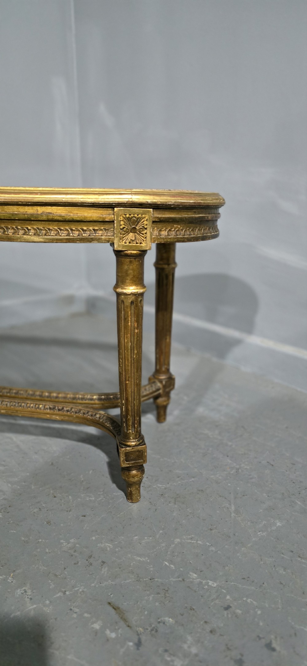 An oval French Louis XVI style duet stool featuring a carved giltwood frame with fluted legs and a gold silk satin upholstered cushion. View VI
