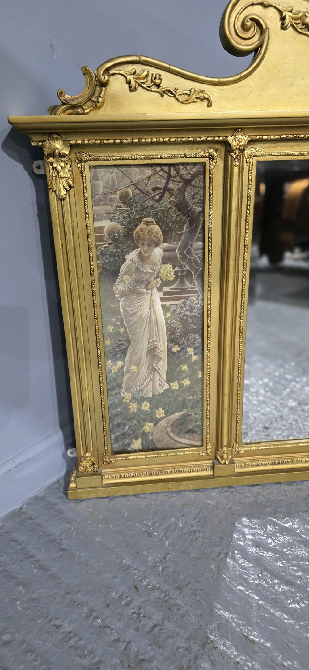An Edwardian giltwood overmantel mirror featuring a central rectangular glass panel flanked by two vertical printed panels depicting classic female figures in garden settings. View II