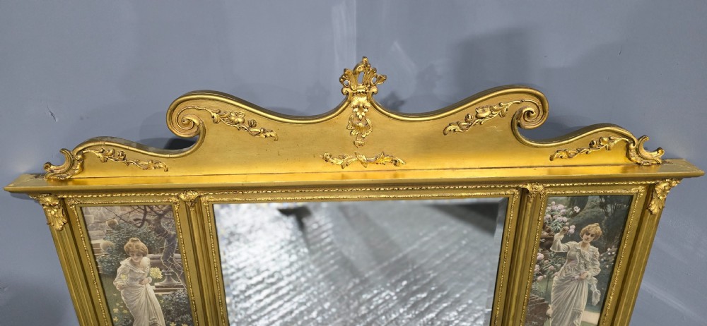 An Edwardian giltwood overmantel mirror featuring a central rectangular glass panel flanked by two vertical printed panels depicting classic female figures in garden settings. View VI