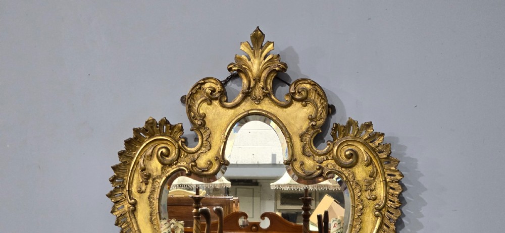 An ornate gold giltwood girandole wall mirror featuring carved Rococo scrollwork and twin integrated candle sconces. View IV