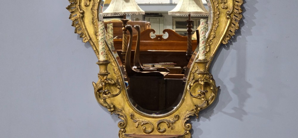 An ornate gold giltwood girandole wall mirror featuring carved Rococo scrollwork and twin integrated candle sconces. View VI