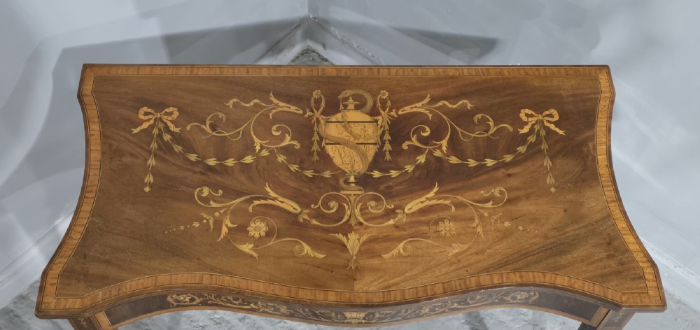 An antique mahogany card table featuring detailed marquetry inlay, a serpentine front, an ornamental urn motif, and square tapered legs. View III