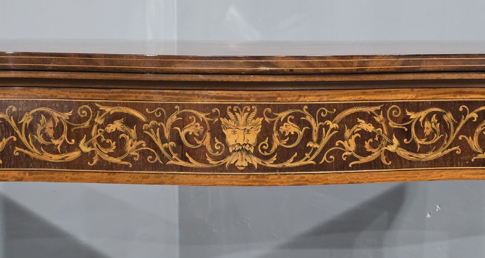 An antique mahogany card table featuring detailed marquetry inlay, a serpentine front, an ornamental urn motif, and square tapered legs. View VIII