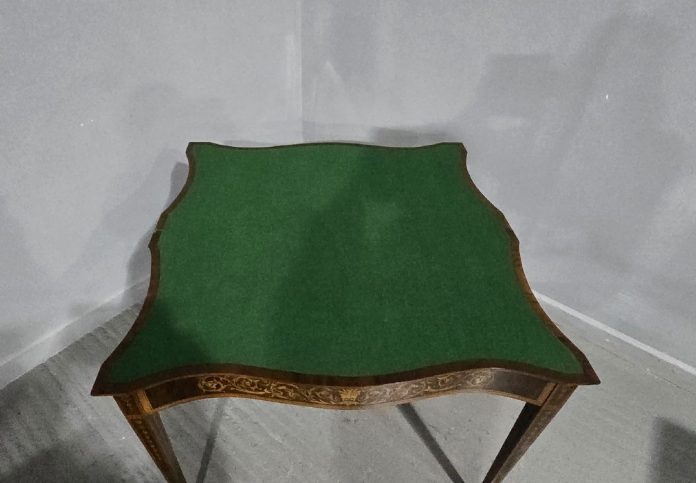 An antique mahogany card table featuring detailed marquetry inlay, a serpentine front, an ornamental urn motif, and square tapered legs. View XIV