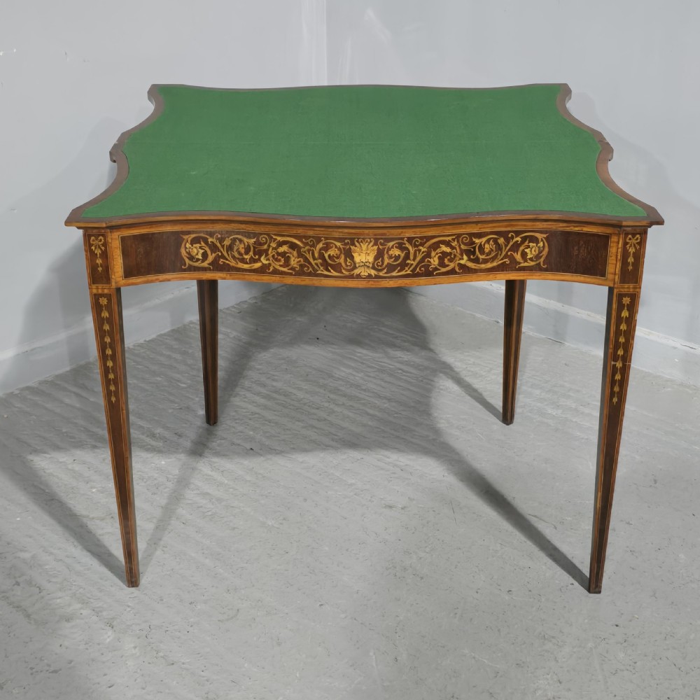 An antique mahogany card table featuring detailed marquetry inlay, a serpentine front, an ornamental urn motif, and square tapered legs. View XVI