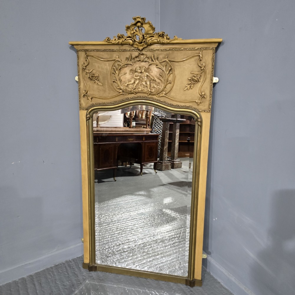 A tall French parcel gilded mirror featuring an ornate floral cresting, a central cherub relief frieze, and a gilded inner border. View II