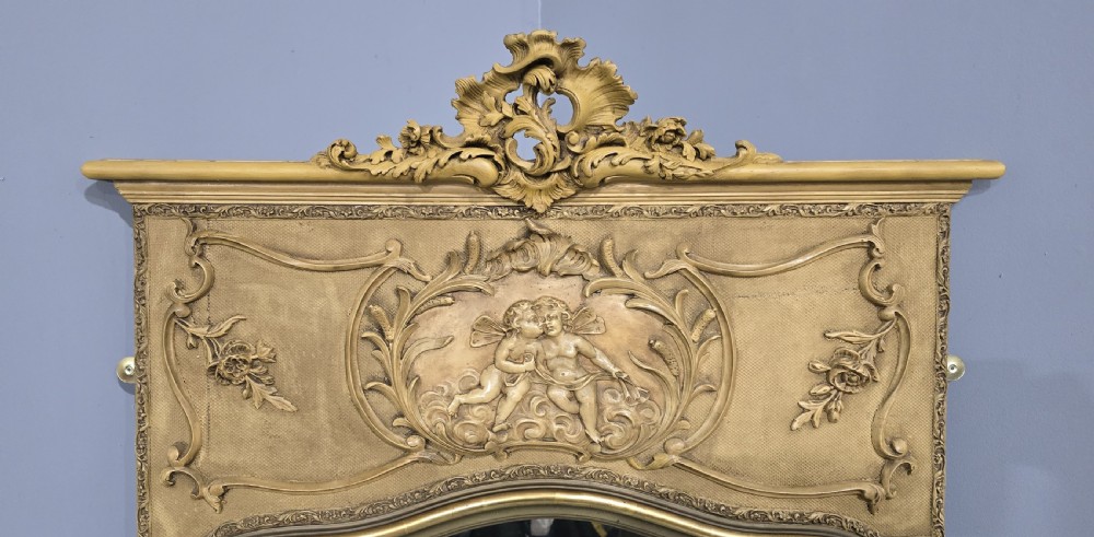 A tall French parcel gilded mirror featuring an ornate floral cresting, a central cherub relief frieze, and a gilded inner border. View III