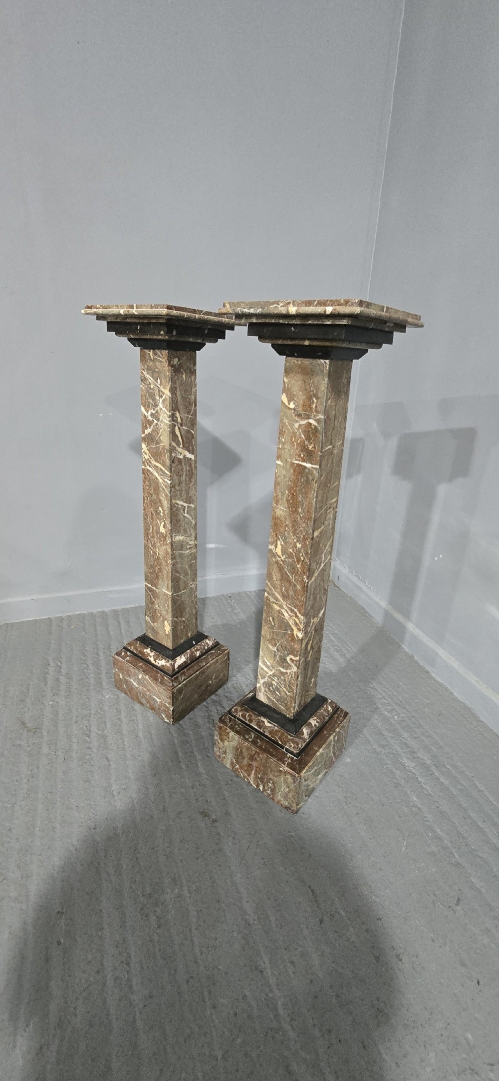 A pair of tall French rouge marble columns with square stepped capital tops, black marble collars, and square plinth bases.