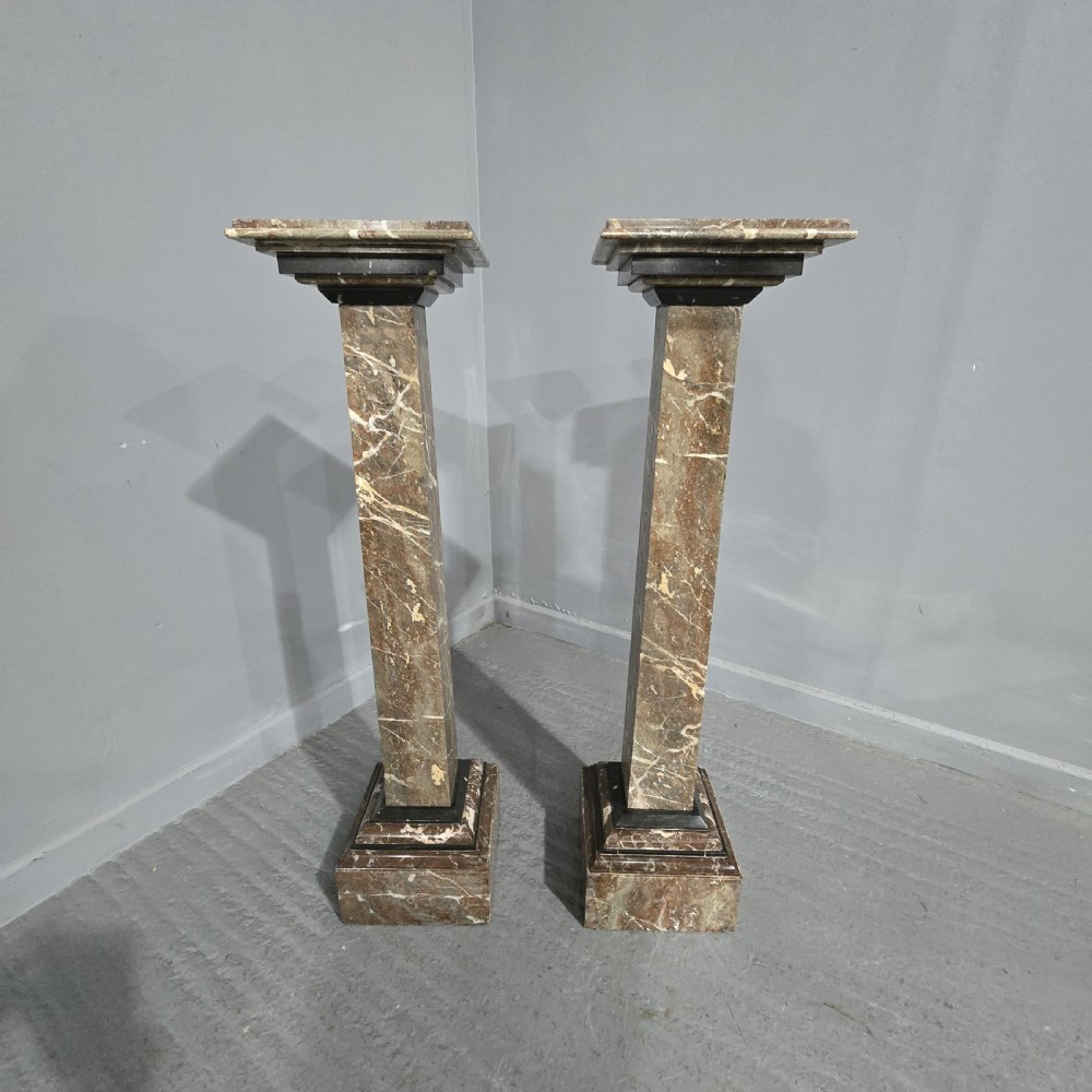 A pair of tall French rouge marble columns with square stepped capital tops, black marble collars, and square plinth bases. View II