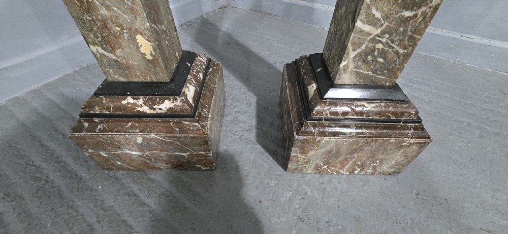 A pair of tall French rouge marble columns with square stepped capital tops, black marble collars, and square plinth bases. View III