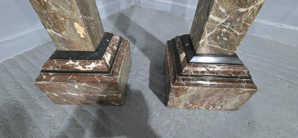 A pair of tall French rouge marble columns with square stepped capital tops, black marble collars, and square plinth bases. View IV
