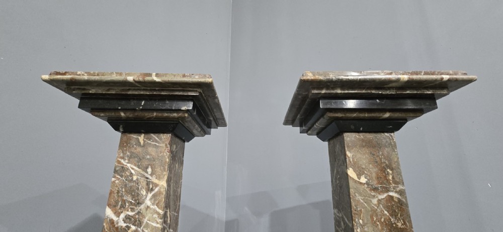 A pair of tall French rouge marble columns with square stepped capital tops, black marble collars, and square plinth bases. View V