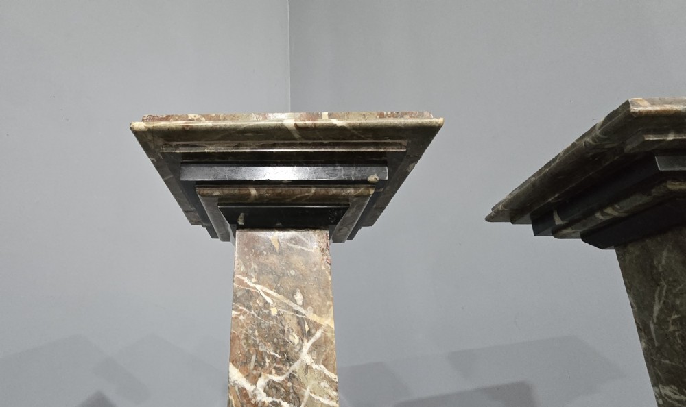A pair of tall French rouge marble columns with square stepped capital tops, black marble collars, and square plinth bases. View VI