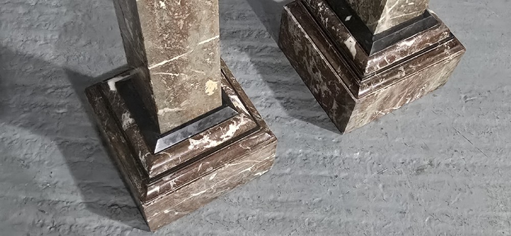 A pair of tall French rouge marble columns with square stepped capital tops, black marble collars, and square plinth bases. View X