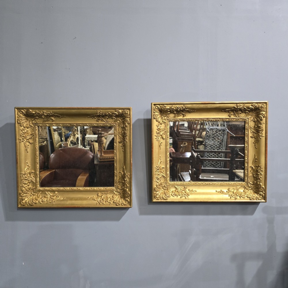 A pair of square antique early Victorian mirrors featuring ornate gold gilt frames with deeply moulded corner scrolls.