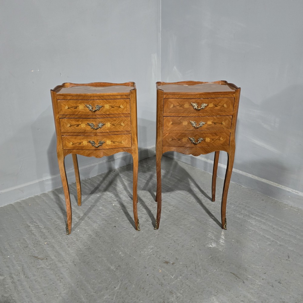 A pair of French marquetry bedside chests with three drawers, floral wood inlays, cabriole legs, and brass handles.