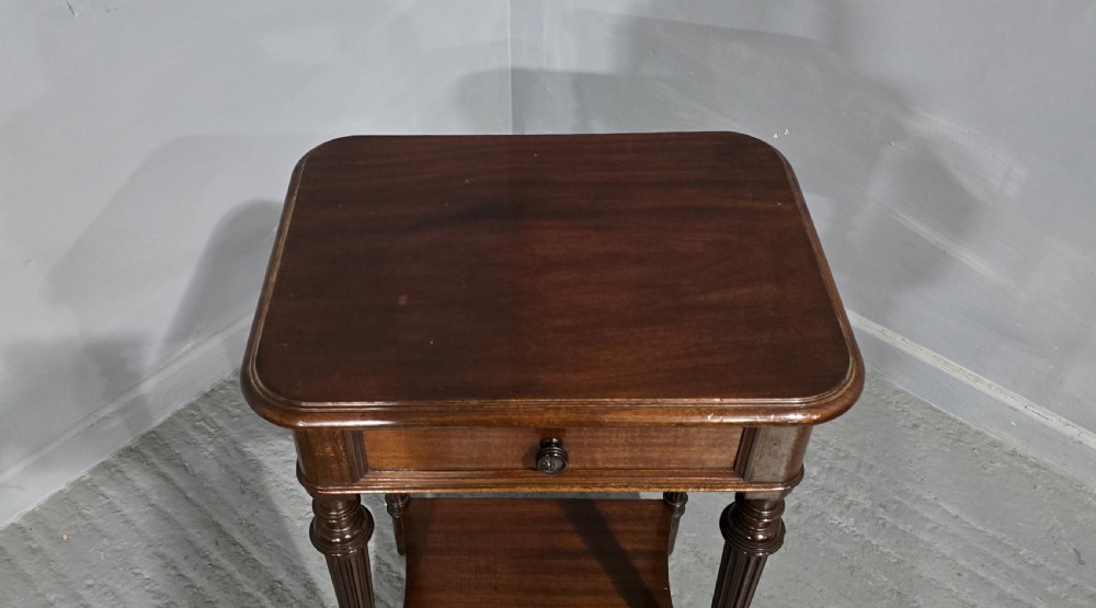 A Victorian mahogany lamp table featuring a single drawer with a round brass knob, four fluted turned legs, and a lower rectangular shelf. View V