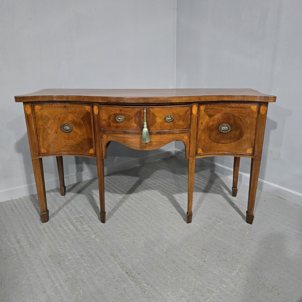 An Edwardian inlaid mahogany sideboard with oval panel doors, central drawers, brass ring handles, and square tapered legs.