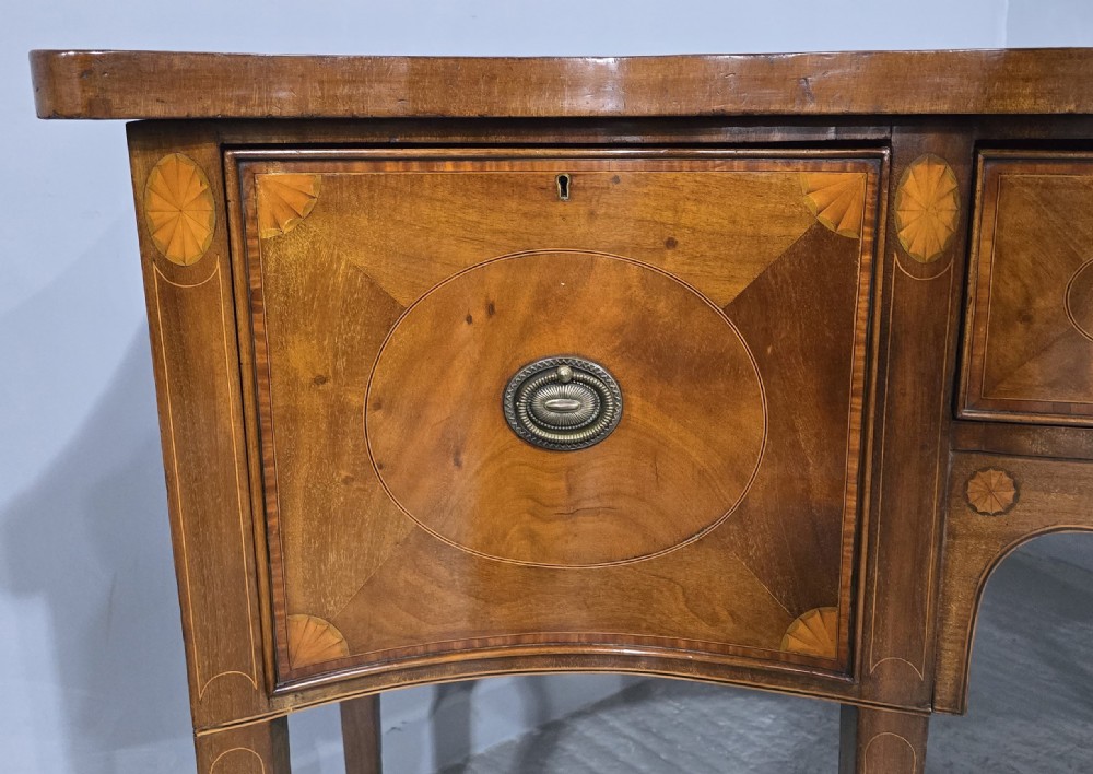 An Edwardian inlaid mahogany sideboard with oval panel doors, central drawers, brass ring handles, and square tapered legs. View V
