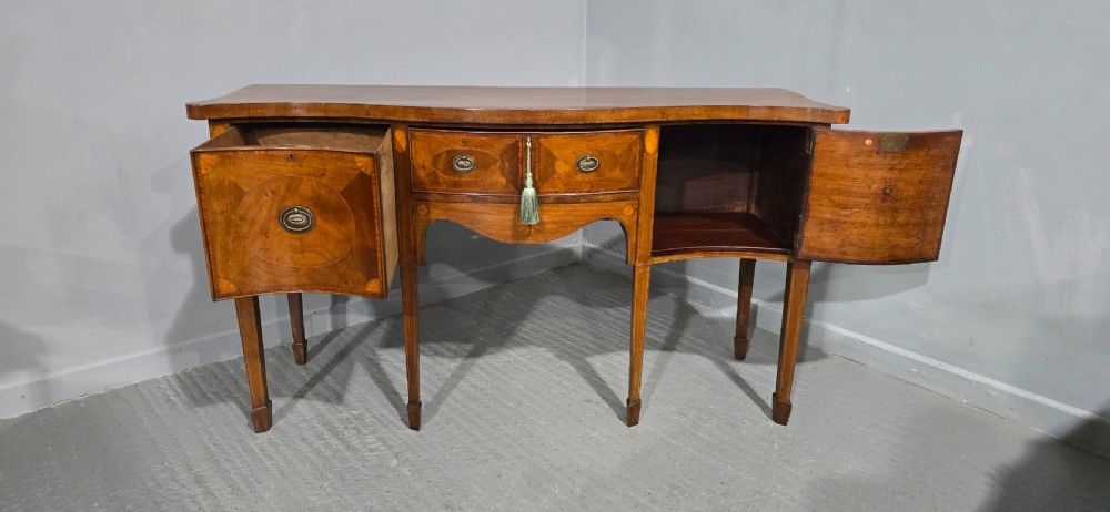 An Edwardian inlaid mahogany sideboard with oval panel doors, central drawers, brass ring handles, and square tapered legs. View XI