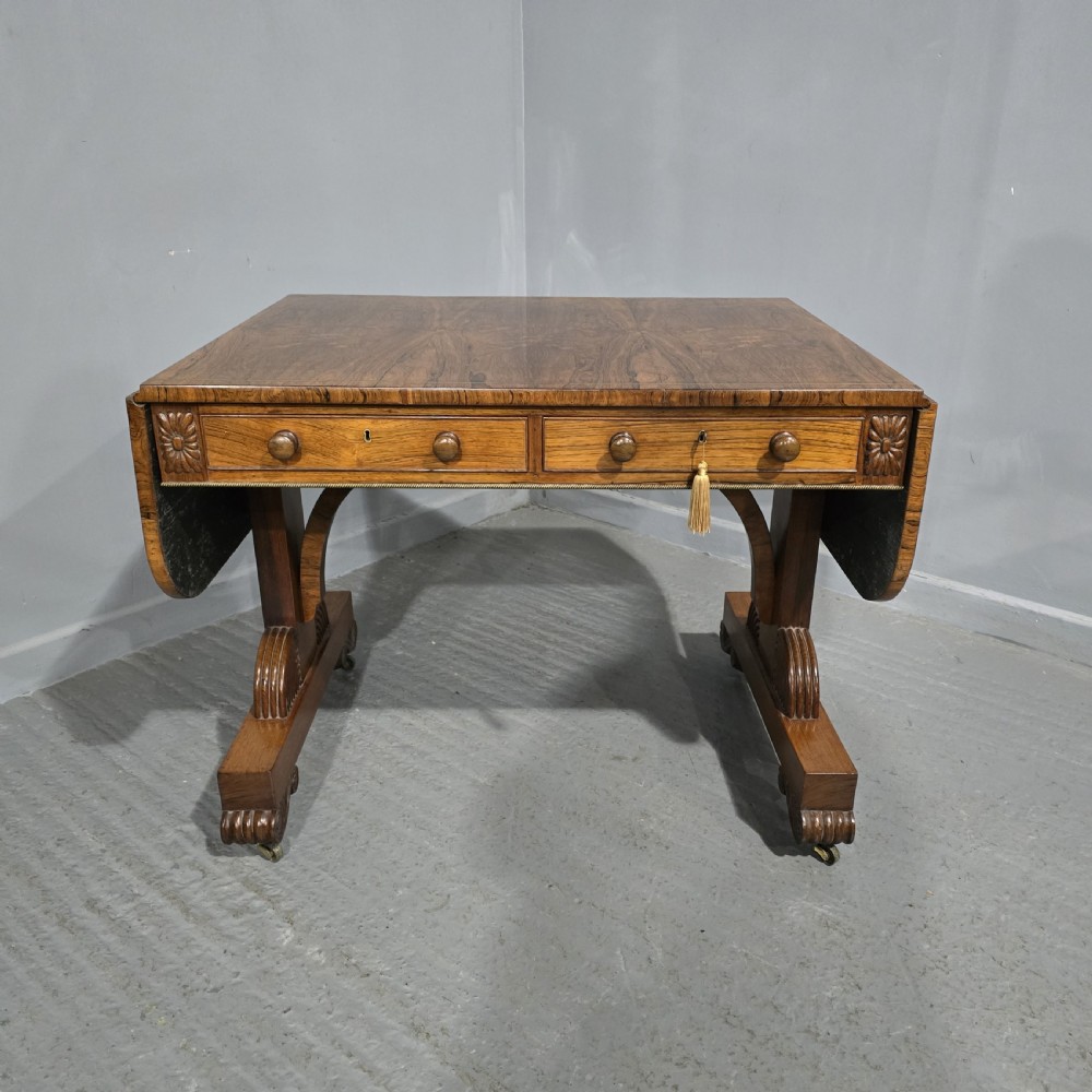 A Regency rosewood sofa table with two frieze drawers, brass line inlay, drop leaves, carved rosette corners, and reeded legs on brass castors.