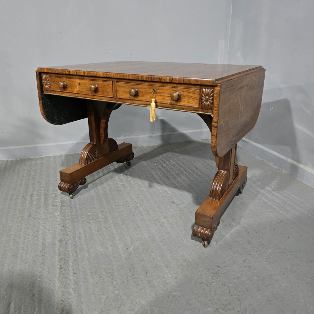 A Regency rosewood sofa table with two frieze drawers, brass line inlay, drop leaves, carved rosette corners, and reeded legs on brass castors. View II