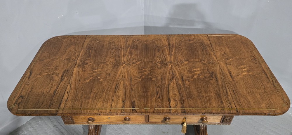 A Regency rosewood sofa table with two frieze drawers, brass line inlay, drop leaves, carved rosette corners, and reeded legs on brass castors. View V