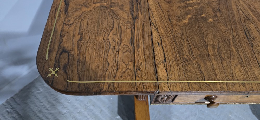 A Regency rosewood sofa table with two frieze drawers, brass line inlay, drop leaves, carved rosette corners, and reeded legs on brass castors. View VI