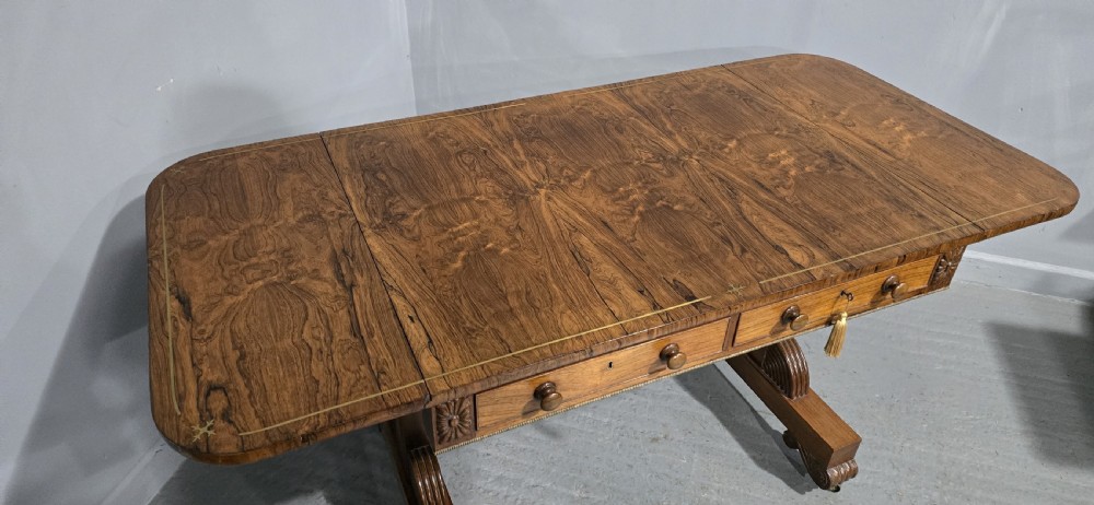 A Regency rosewood sofa table with two frieze drawers, brass line inlay, drop leaves, carved rosette corners, and reeded legs on brass castors. View VII