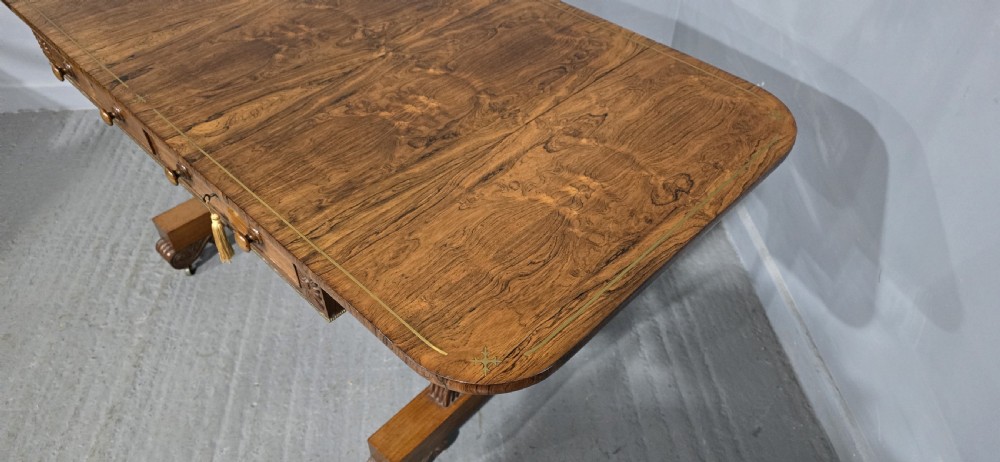 A Regency rosewood sofa table with two frieze drawers, brass line inlay, drop leaves, carved rosette corners, and reeded legs on brass castors. View IX