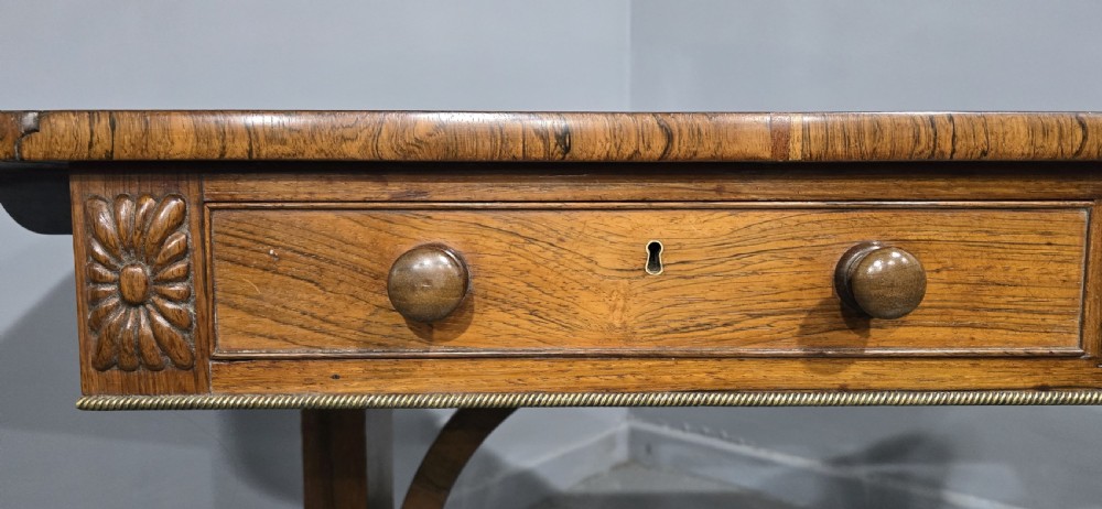 A Regency rosewood sofa table with two frieze drawers, brass line inlay, drop leaves, carved rosette corners, and reeded legs on brass castors. View XV