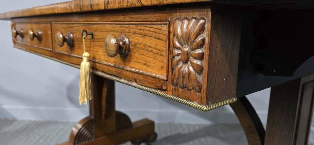 A Regency rosewood sofa table with two frieze drawers, brass line inlay, drop leaves, carved rosette corners, and reeded legs on brass castors. View XVIII