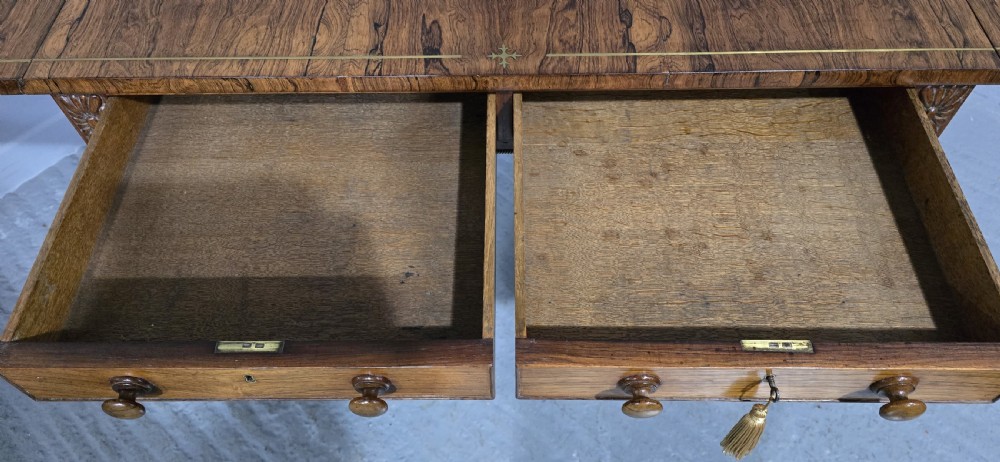 A Regency rosewood sofa table with two frieze drawers, brass line inlay, drop leaves, carved rosette corners, and reeded legs on brass castors. View XX
